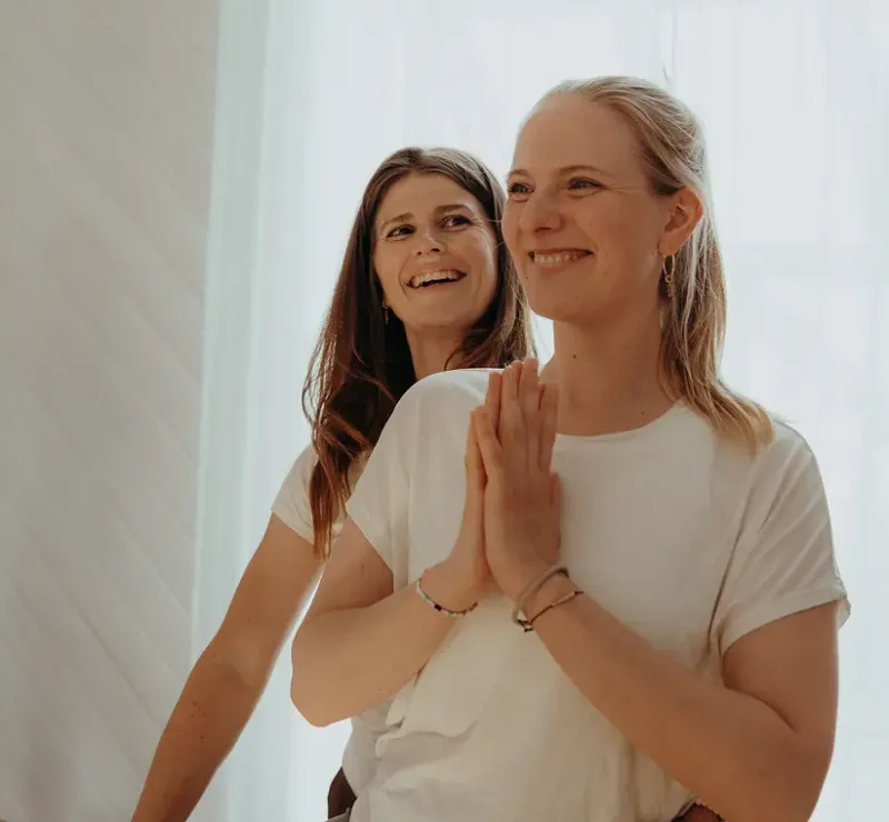 Zwei lächelnde Frauen beim Yoga mit Händen vor dem Herzen